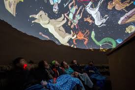 Several people sitting under a projection of the cusco night sky